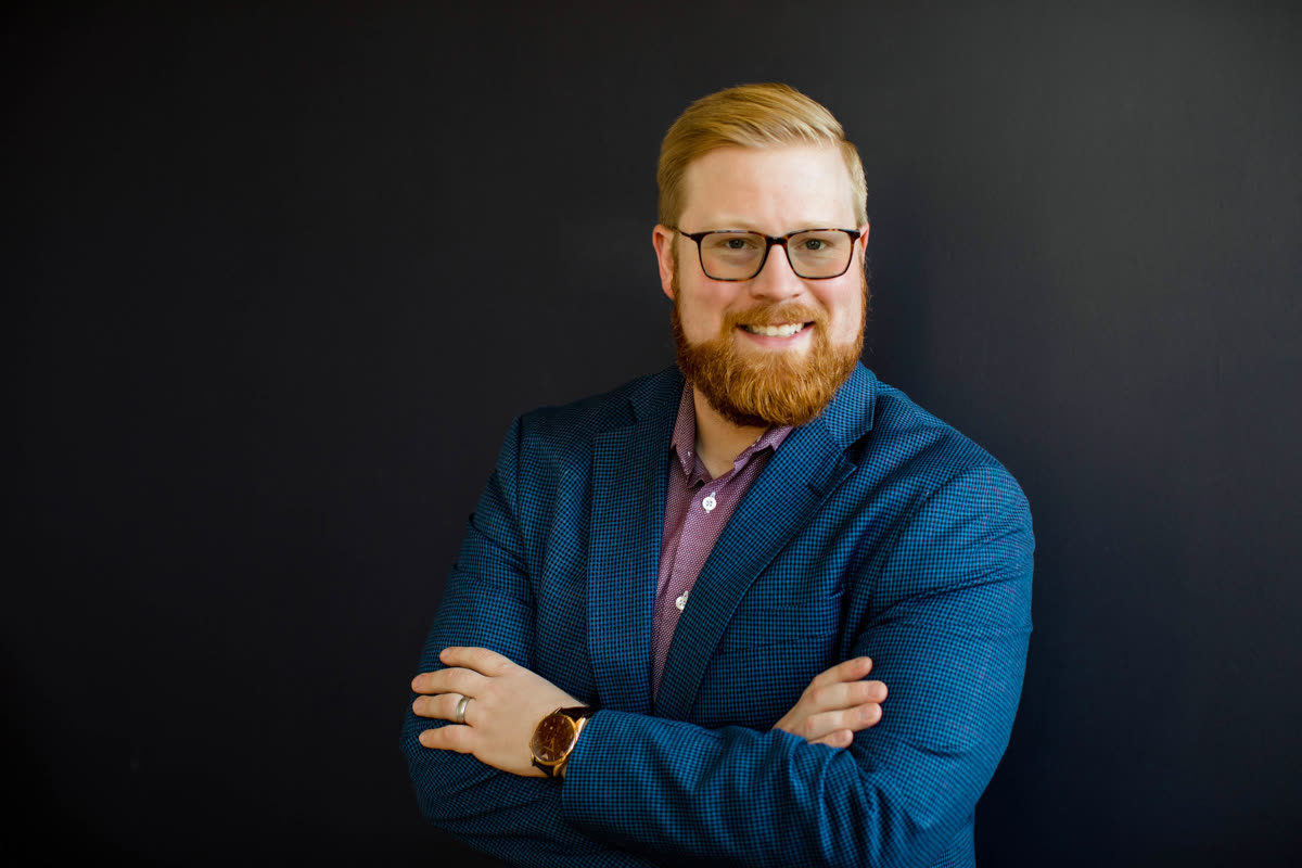 Ryan Kirk in a dark blazer against a neutral dark background